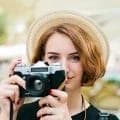 A woman in a straw hat taking a photo with a vintage film camera