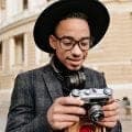 A man in a black hat and glasses looking down at a film camera