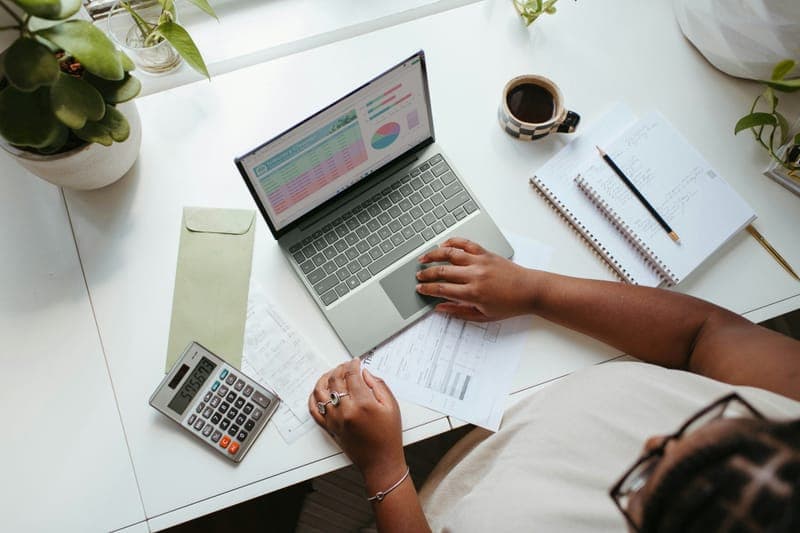 Hands typing on a laptop at a white desk with a calculator, notebook and coffee