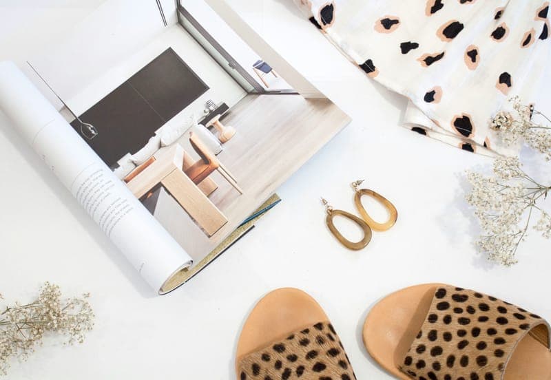 A fashion magazine, gold earrings and leopard-print sandals on a white table