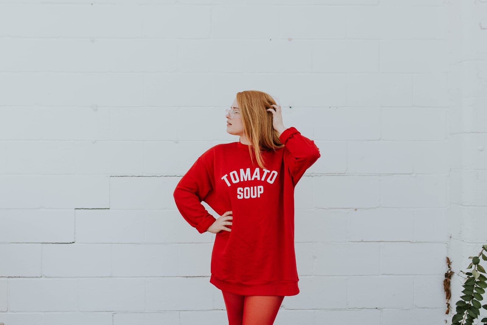 A woman in a red sweater dress posing against a white brick wall
