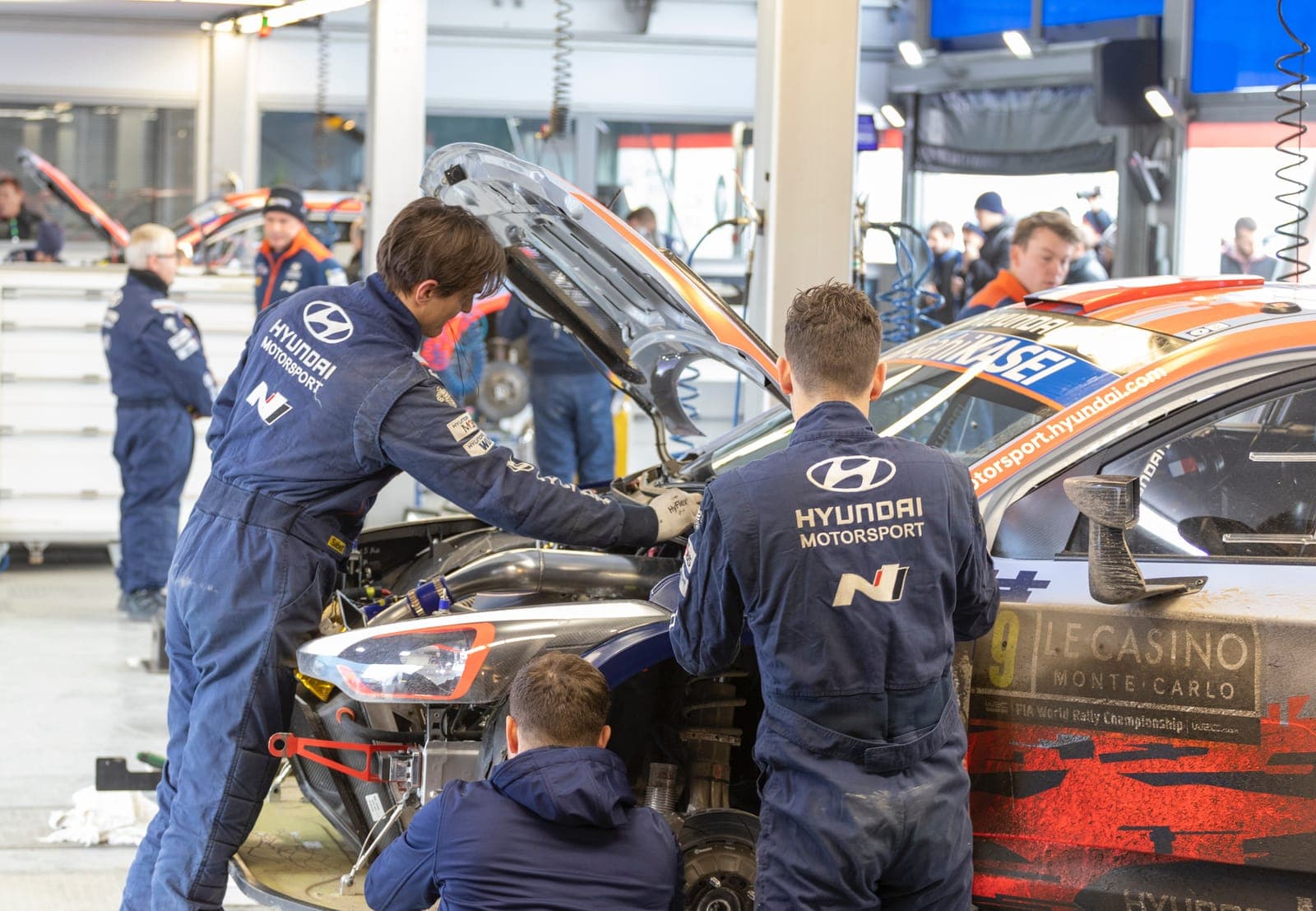 Mechanics in team overalls working on a rally car in the pits