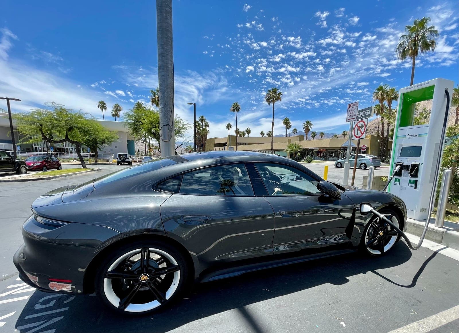 A dark grey electric sports car at a charging station under palm trees