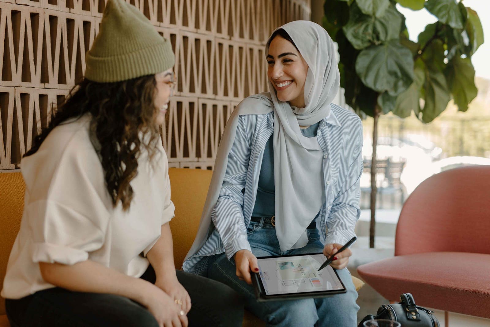 Two women talking in a lounge, one holding a tablet
