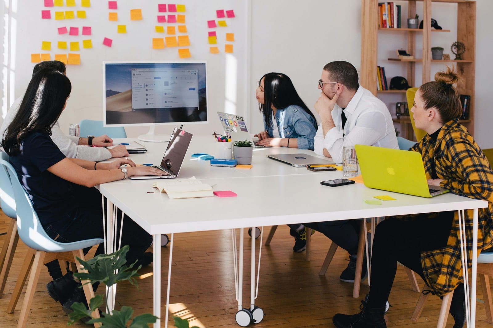 A team working on laptops around a white table in an office with sticky notes