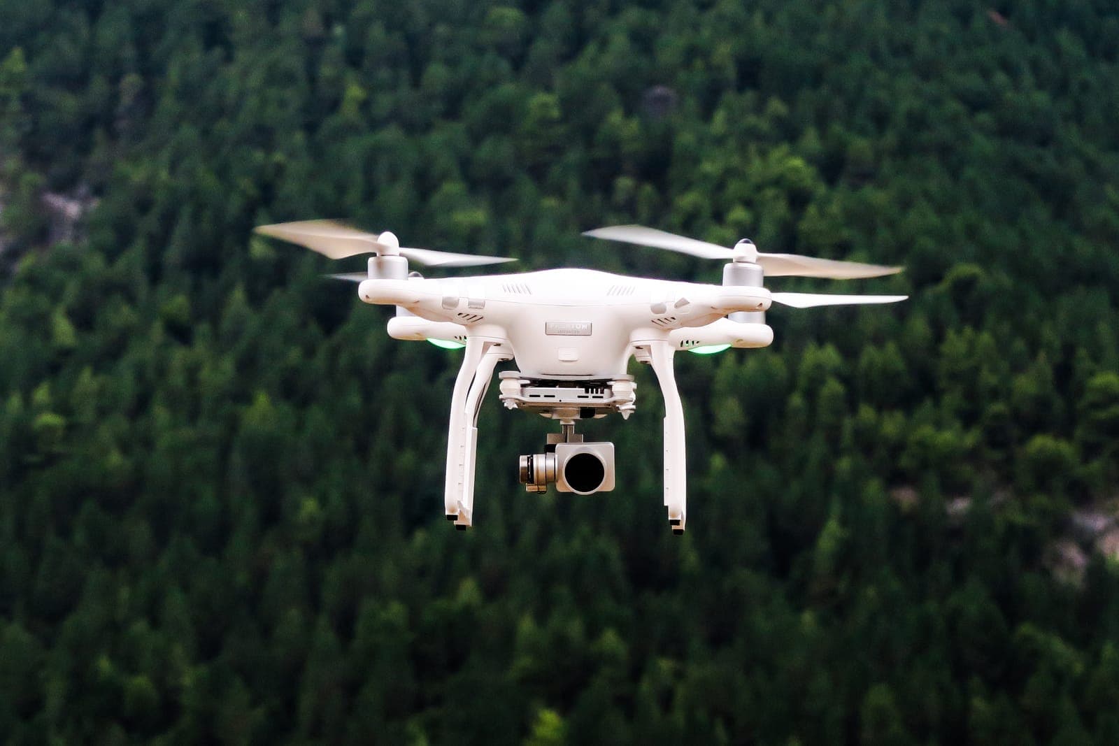 A white drone flying over a pine forest